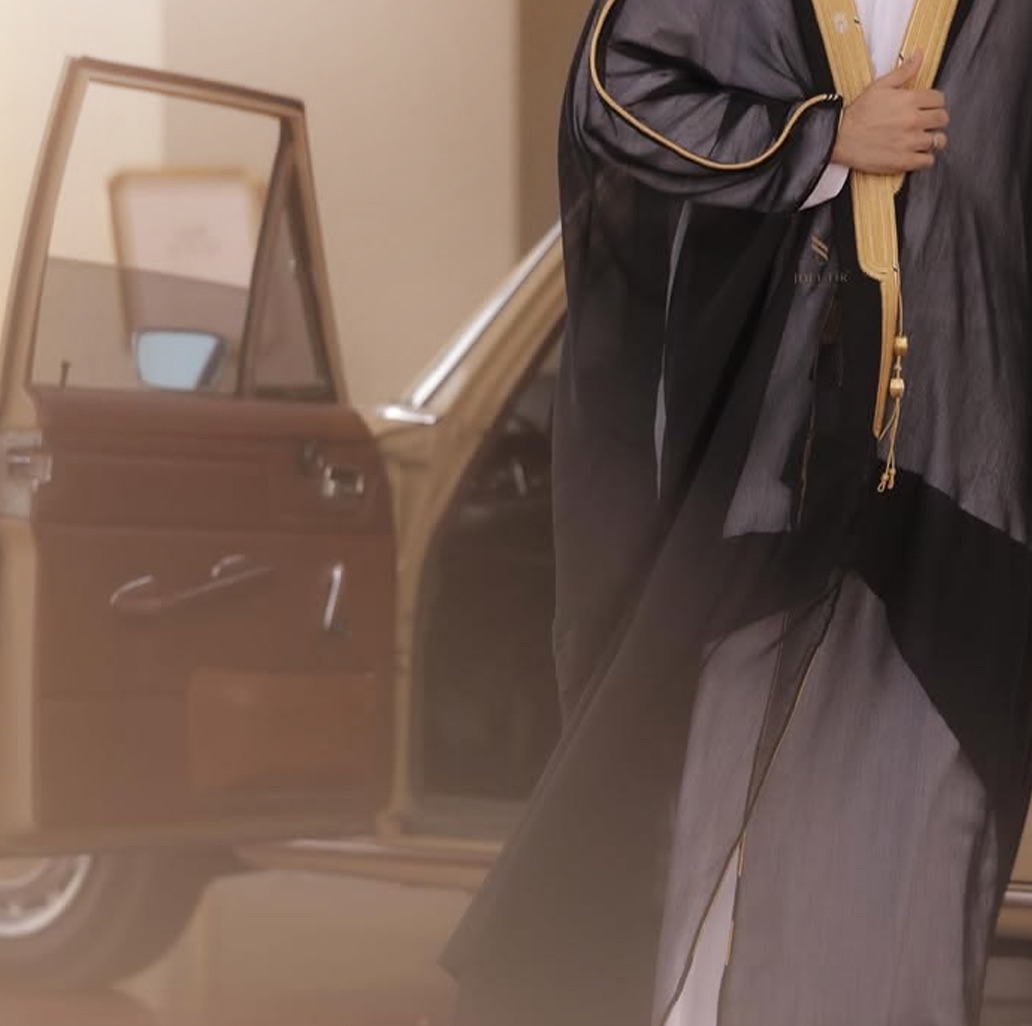 A figure in a black-and-gold bisht stepping out beside a classic car